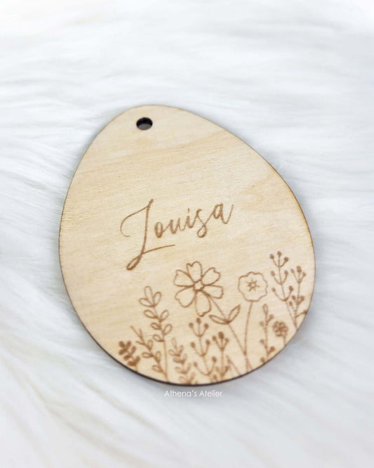 Personalisierter Geschenkanhänger aus Holz in Eiform mit filigraner Wildblumen-Wiese und Wunschname – Athena's Atelier.