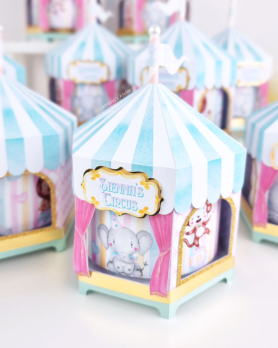 Personalized circus tent carousel spinning centerpiece in light blue and pink with hand-drawn animal illustrations by Athenas Atelier.