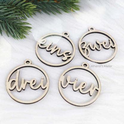 Set aus vier runden Adventszahlen aus hellem Holz, mit den Wörtern eins, zwei, drei, vier in eleganter Schreibschrift lasergeschnitten.