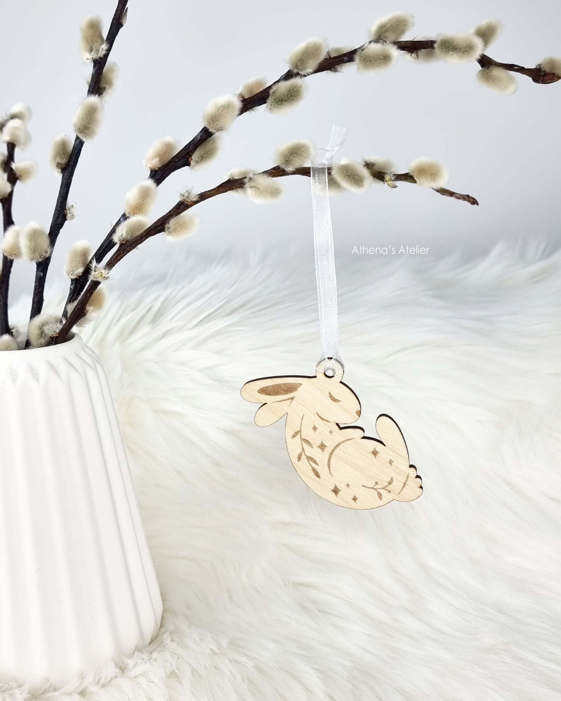 Drei schlafende Osterhasen-Anhänger aus Holz, dekorativ hängend an einem Palmkätzchen-Zweig als traditioneller Osterstrauß – Athena's Atelier.