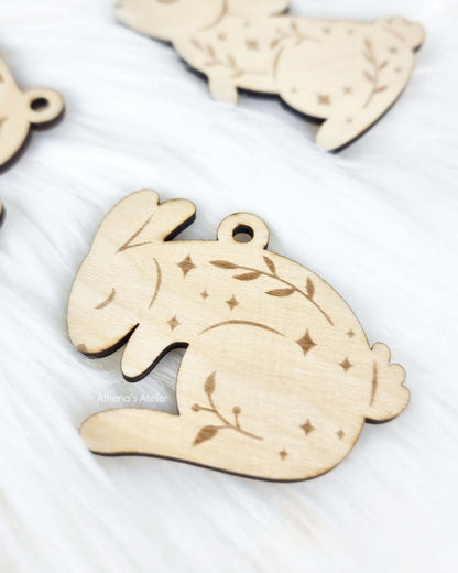 Set aus drei handgefertigten Holz-Anhängern in Hasenform mit filigraner Gravur von Zweigen und Sternen für die Osterdekoration – Athena's Atelier.